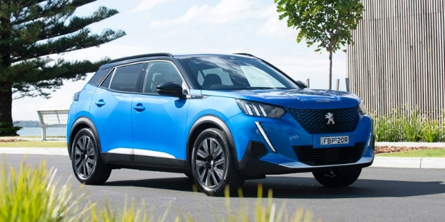 Side-angle view of a blue Peugeot driving along a road.