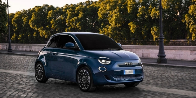 A side-angle view of a blue Fiat 500e driving along a road.