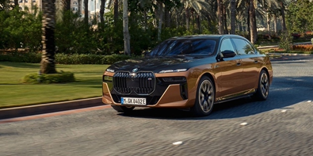 A BMW i7 xDrive60 drives through a palm tree-lined street