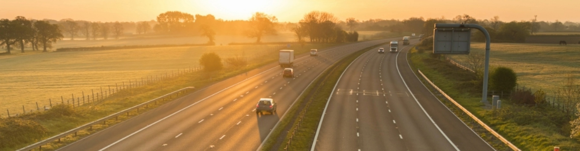 Ariel view of vehicles travelling along a highway toward a golden sunset.