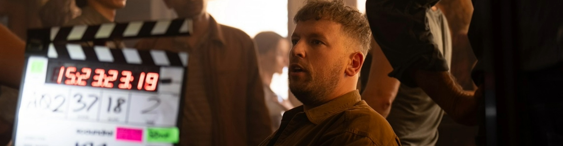 Wheelchair tennis champion Dylan Alcott in a dimly lit room with lots of people around and a digital clapperboard being held up near him.