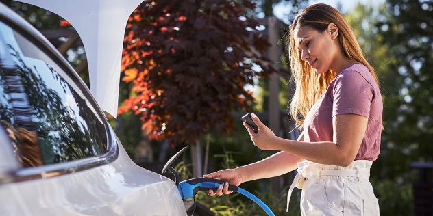 woman putting charger into her EV holding mobile phone