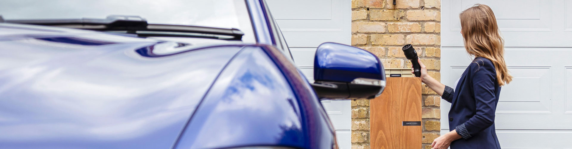 woman-using-ev-charger-at-home-1920x500 Woman charging an EV in front of a garage