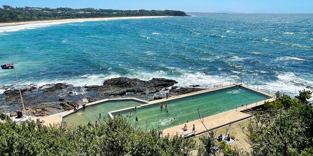 View of Black Head Ocean Pool on a sunny day with ocean in the background from a hill above the bay near Hallidays Point