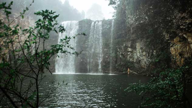 A person stands in the distance next to Dangar Falls contemplating jumping in