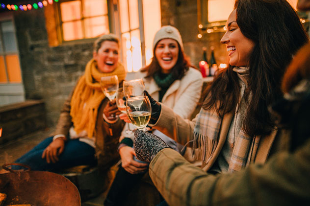 Three mothers sit laughing with glasses of white wine in hand