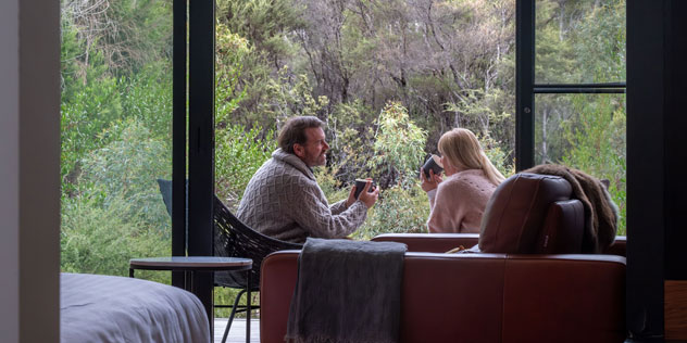 A couple sit by a large glass window looking at trees at Freycinet Lodge