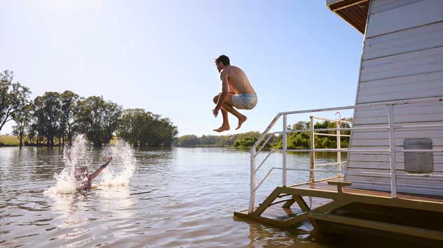 A person jumps into a river from a house boat