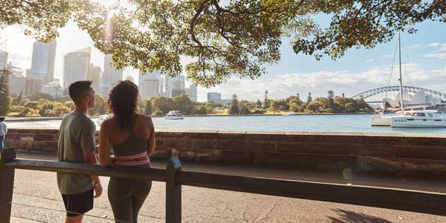 A couple stands looking at the harbour from Sydney's Botanic Gardens
