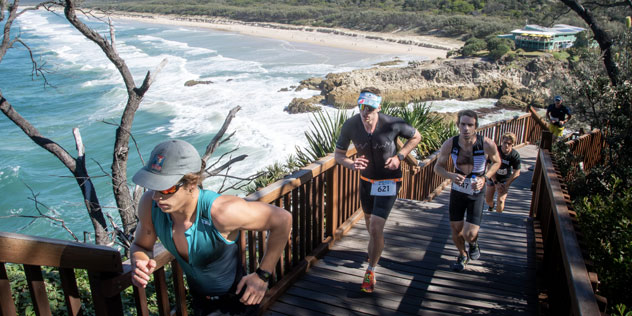 People running up stairs in front of beach - Straddie Salute Triathlon Festival