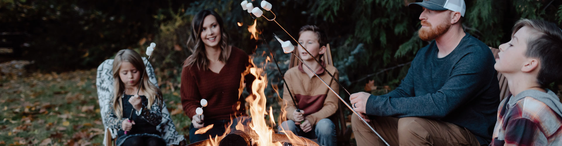 A family sits around a campfire in a copper brazier toasting marchmallows