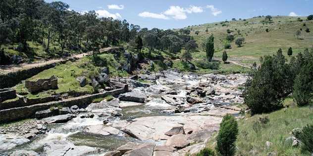 stony riverbed that winds through tree-covered hillside with ruins of small brick buildings on the riverbank