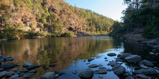 Rocks along the edge of a pool of water at the bottom of scrubby hillsides dotted with trees.