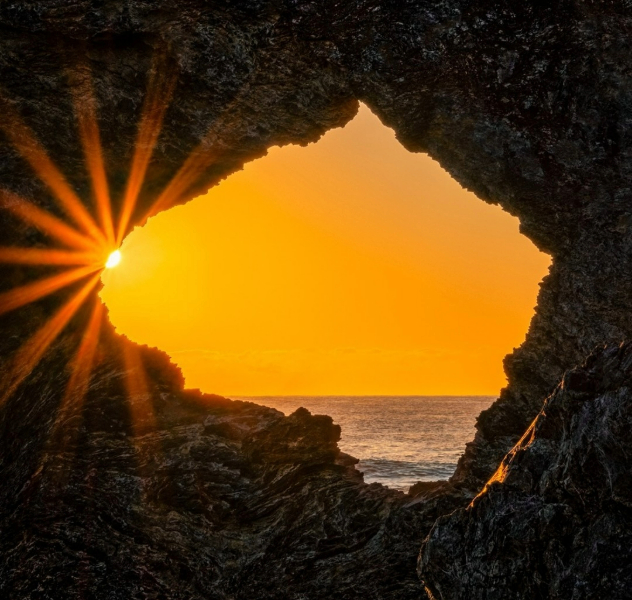 A orange sunset over the sea seen through a rocky hole shaped like continental Australia. 