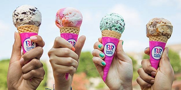 four hands holding waffle ice cream cones with Baskin Robbins advertising sleeves in a range of flavours including cookies and cream, fruit, choc mint and caramel