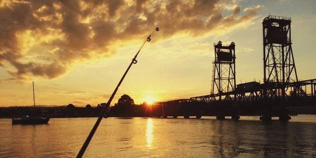 sunset silhouette of bridge with fishing rod in the foreground