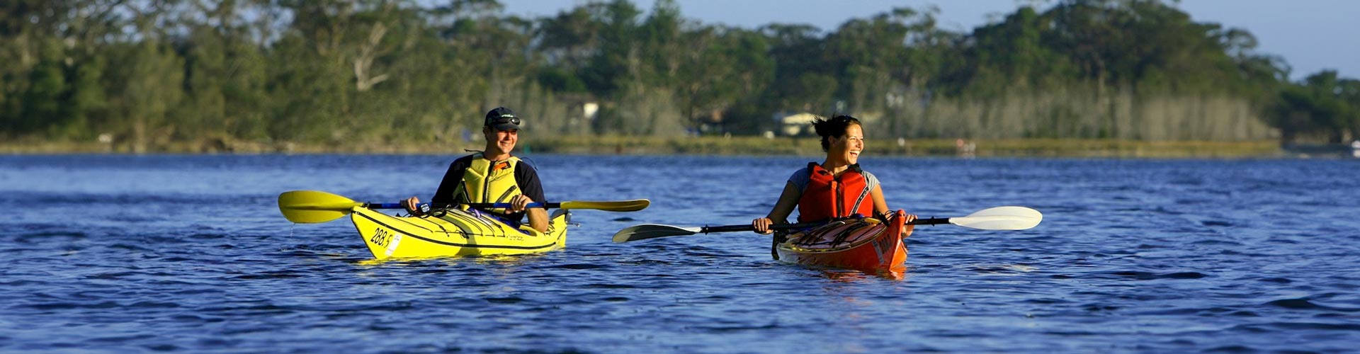 Two women kayaking on a lake in the late afternoon sun
