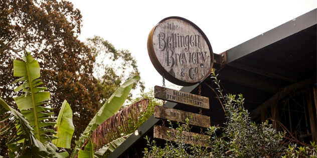 The Bellingen Brewery’s round wooden sign, affixed to the apex of a roof, with tropical foliage in the background. 