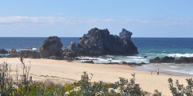 wide sandy beach with volcanic rock formation in the shape of a now headless camel, known as camel rock that joins the beach to the sea