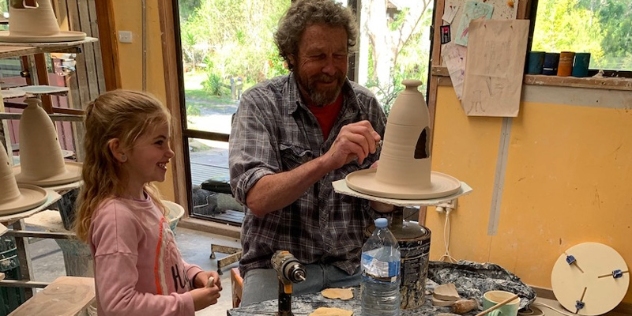 young girl watches a skilled potter putting the finishing touches to a clay salt pot