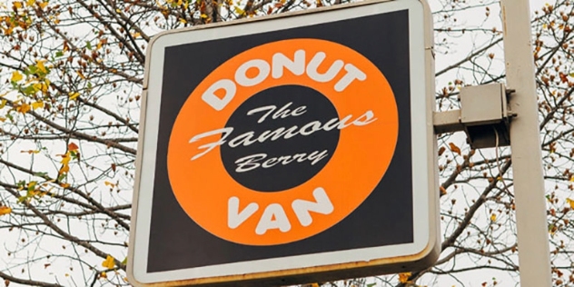 signpost with logo consisting of bright orange donut on a brown background with the famous donut van written on it