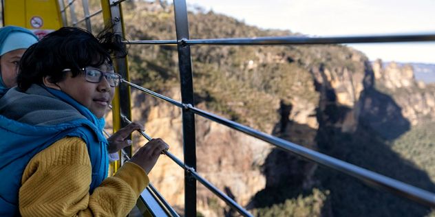 Teens look out from a cable car window over a vast mountain gorge.