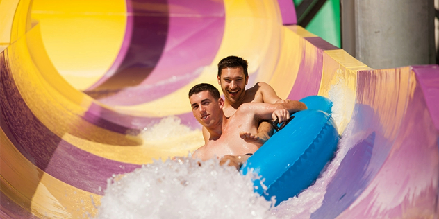  Two teen boys ride a tube down a yellow and purple striped slide at Wet n' Wild Gold Coast.