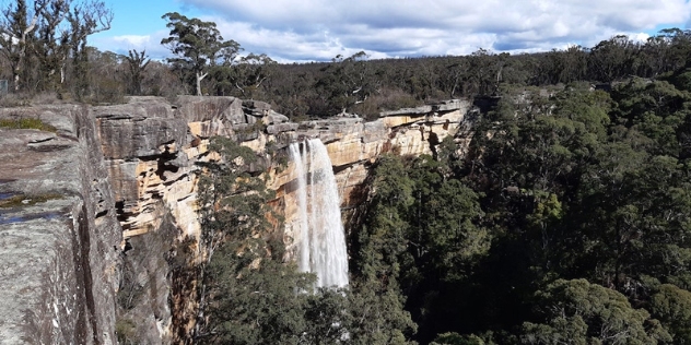 waterfall spills impressively from the top of a cliff face of grey weathered rocks