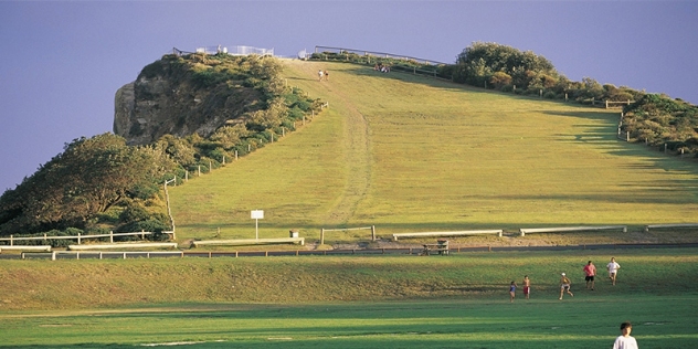 green hill leading to a headland with two distant people walking towards the lookout