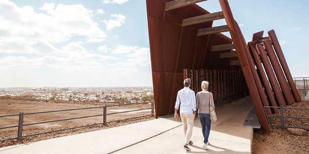 man and woman walking between the rust-coloured metal archway where lists of names commemorate miners who have died