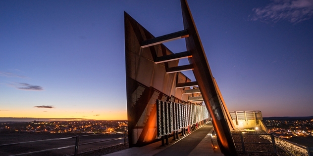 dusk view of metal monument with the lights of the town in the background