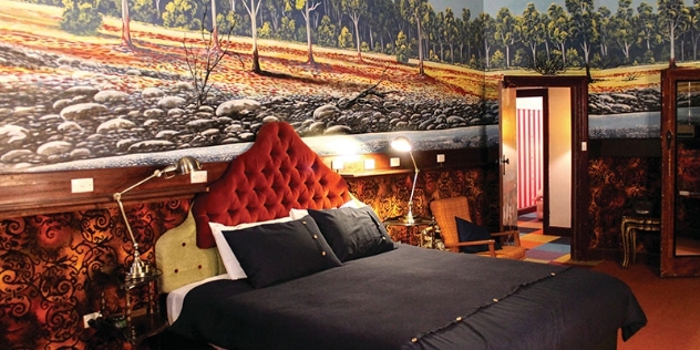 maximalist decor with a rust orange velvet headboard and walls decorated with a rural mural and 70s orange and brown carpet