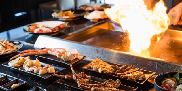 meat and seafood teppanyaki dishes in the foreground with flame over hot plate behind