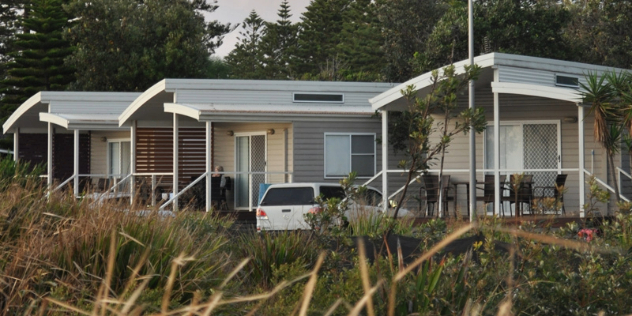  A row of matching modern cabins, framed by trees along a grassy lakeshore.