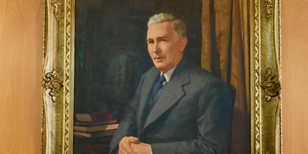  An oil portrait of a grey haired, clean shaven man in a suit, with a gold gilded frame. 