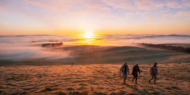 Three hikers walking over misty hills as the sunrises