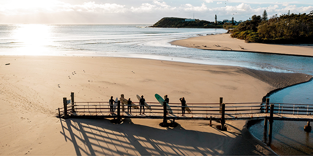 silhouette of surfers on a pier against a beach