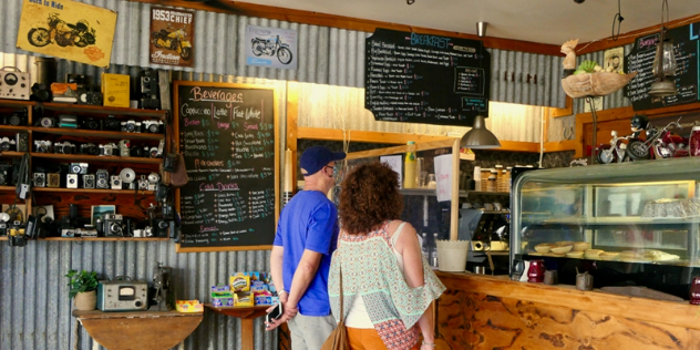 A couple at a wooden cafe counter with corrugated iron walls covered with vintage posters and antique cameras.