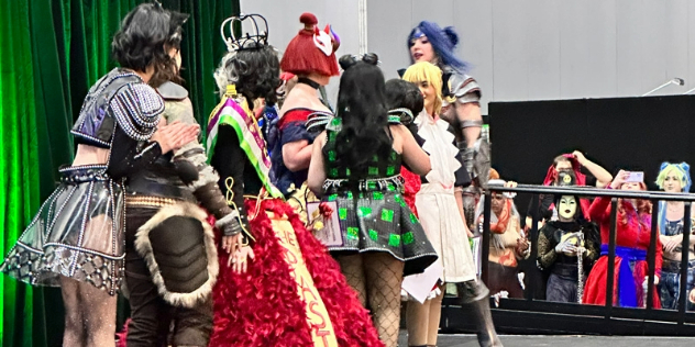 A group of cosplayers dressed as popular feminine anime characters gather inside a convention.