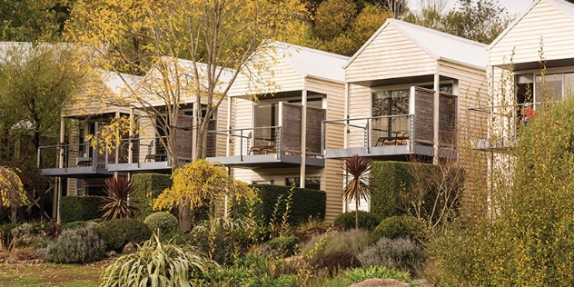 row of weatherboard, two storey lodges with balconies overlooking manicured gardens next to a lake