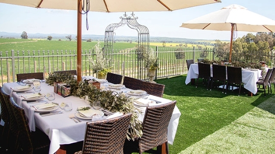 stylishly laid outdoor tables with white linen tablecloths and each with a sun umbrella overlooking green fields