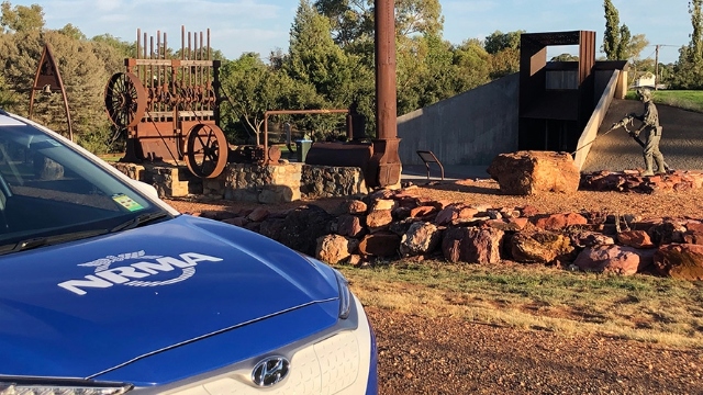 ev Cobar Miners Heritage Park NSW NRMA electric vehicle parked next to exhibit of old machinery and a sculpture of a miner
