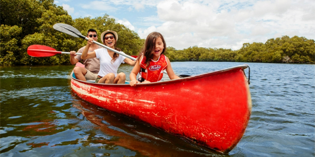  A couple and young girl in a canoe together smiling as they paddle near mangrove trees.