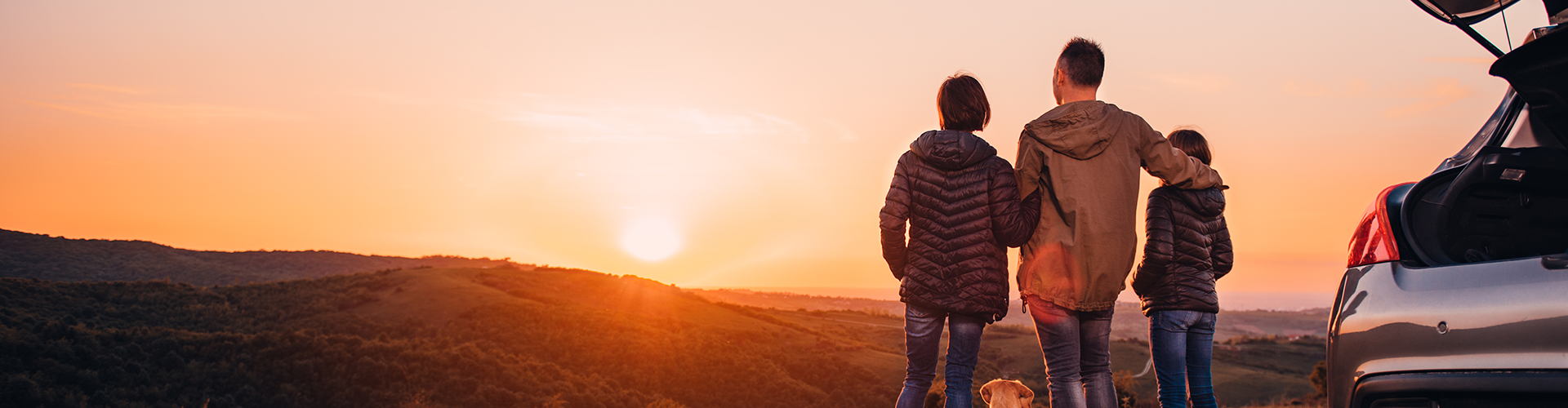 A family watching the sunset next to the open boot of their car