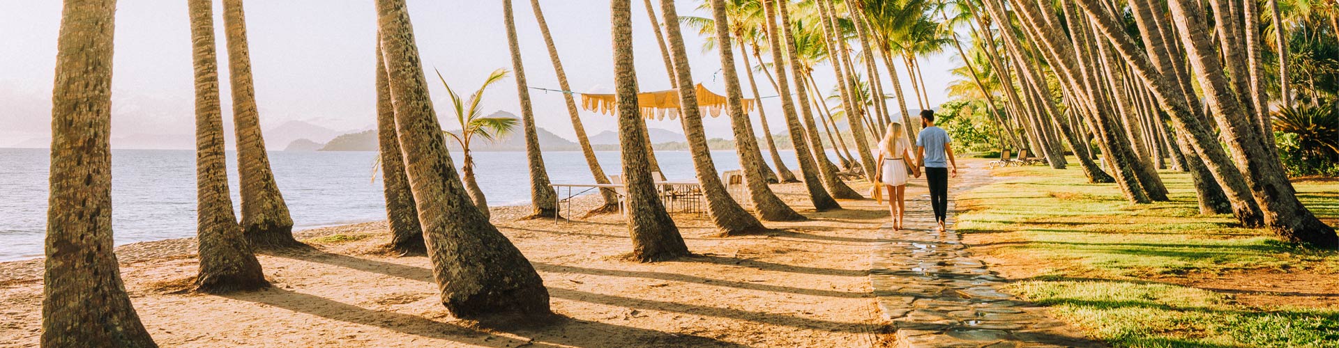 A couple walks under palm trees at Palm Cover, Far North Queensland