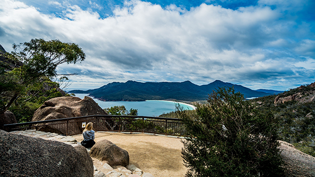 A woman sitting on a rock, taking in the view of Wineglass Bay from Wineglass Bay Track Lookout