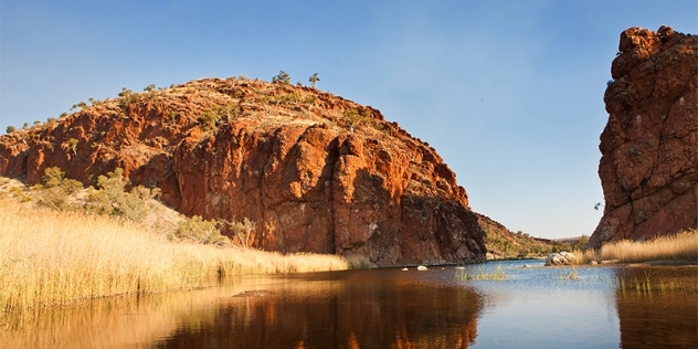 wide creek flanked by grasses and large orange rock formations