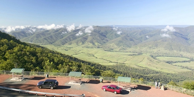 arial view of cars and people at a lookout over a valley of trees with hills in the distance