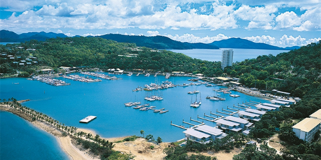  Boats moored in a square shaped harbour created by sand walls, surrounded by dense rainforest trees.