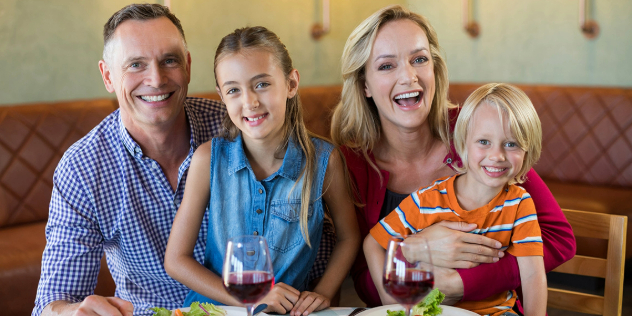  A mother, father, girl and boy sitting at a restaurant table, laughing and smiling.